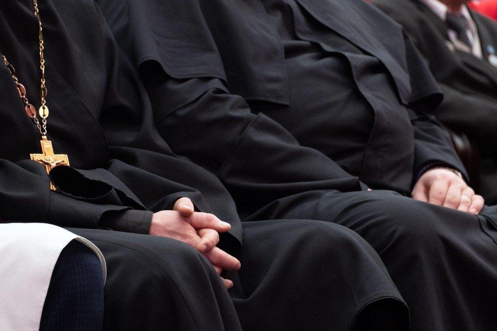 Representatives of the Orthodox clergy in black robes sit in the conference hall.