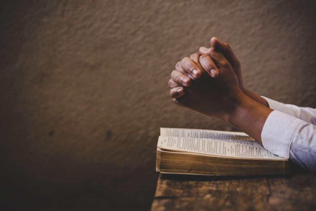 Folded hands in prayer over a bible.