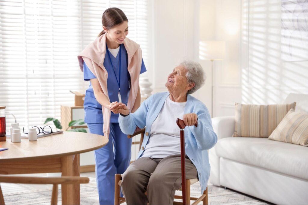 Caregiver supporting senior woman indoors. Home health care service.