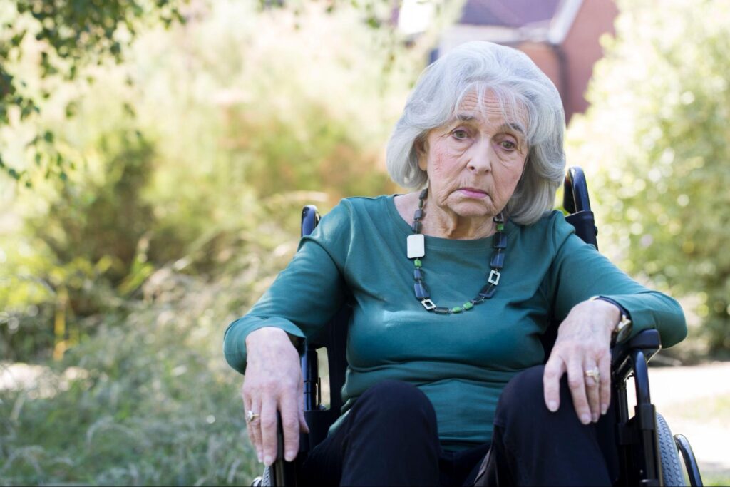 Depressed Senior Woman In Wheelchair Sitting Outdoors.