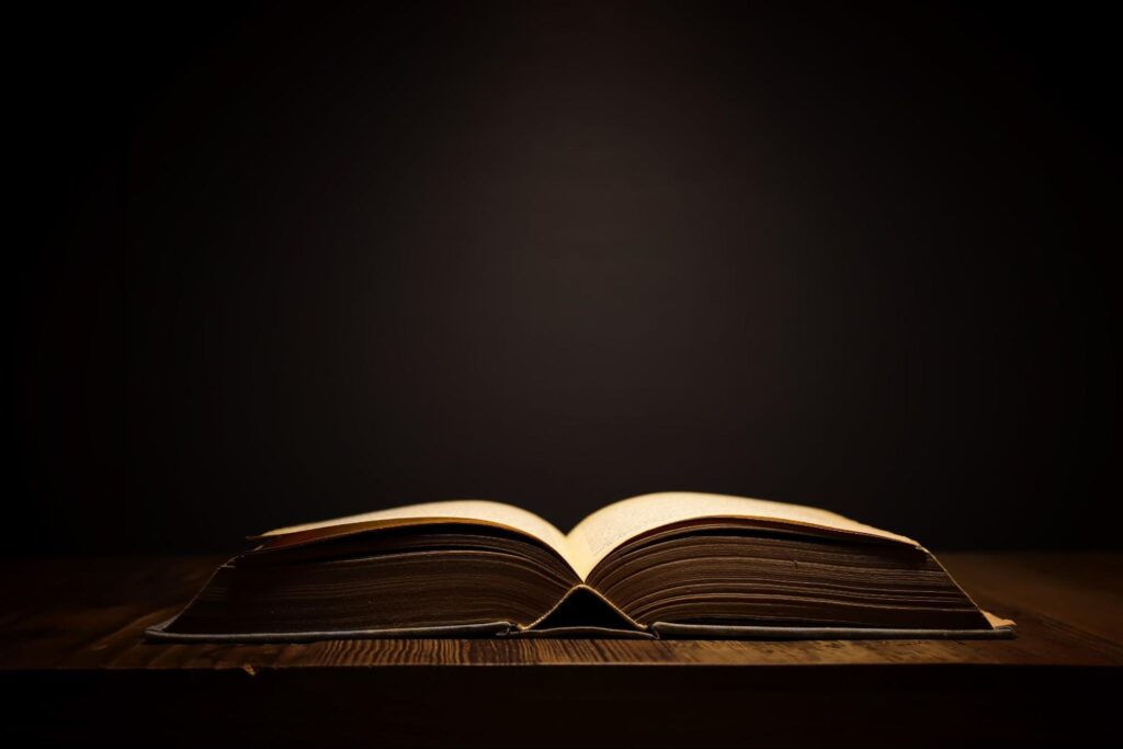 Image of open antique book on wooden table with dark background.
