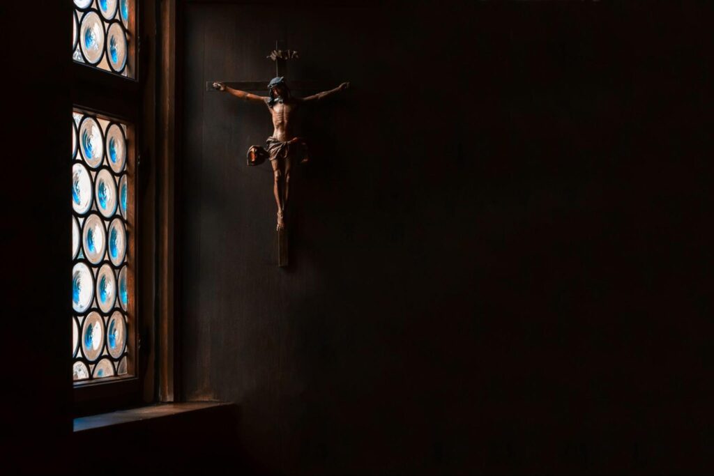 The crucifix, a cross with Jesus hanging on the wall, rays of light gently illuminate it.