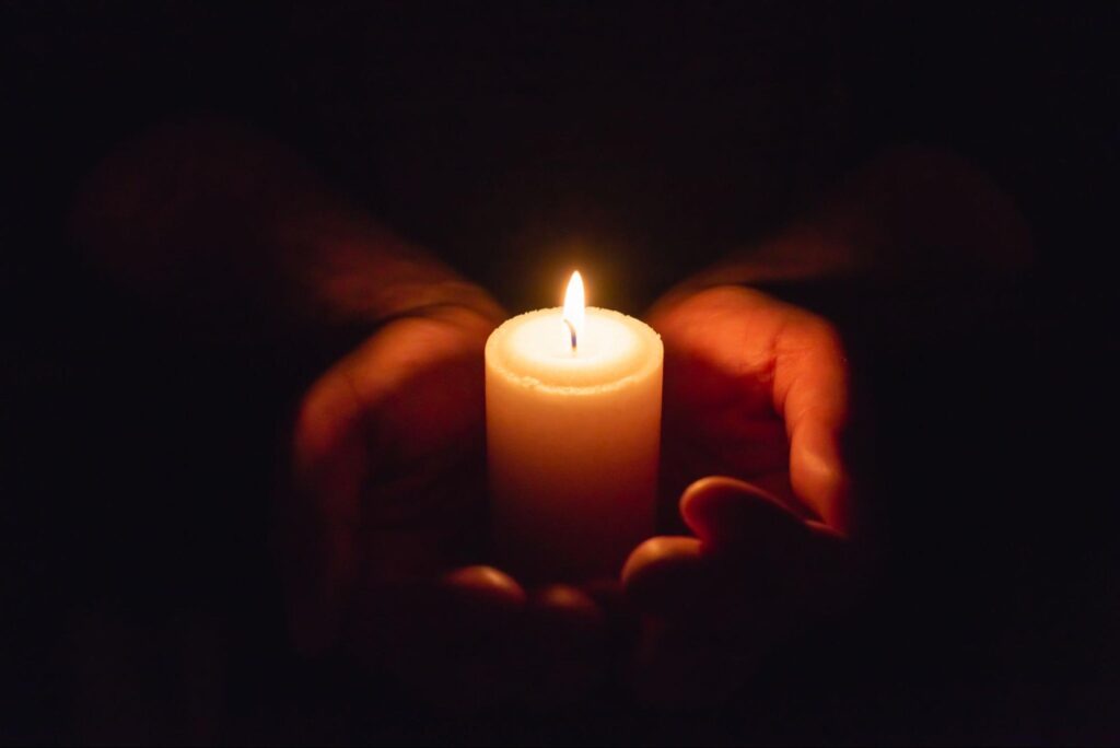 Hands holding burning candle in dark like a heart.